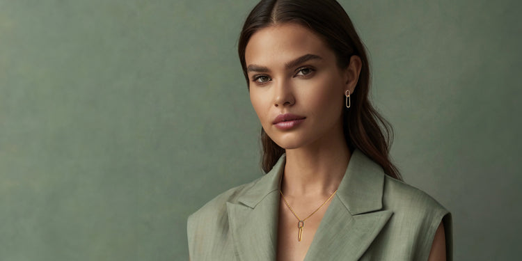 Elegante Frau in olivgrünem Blazer mit braunen Haaren trägt bronzene Halskette mit Anhänger und passende Ohrringe