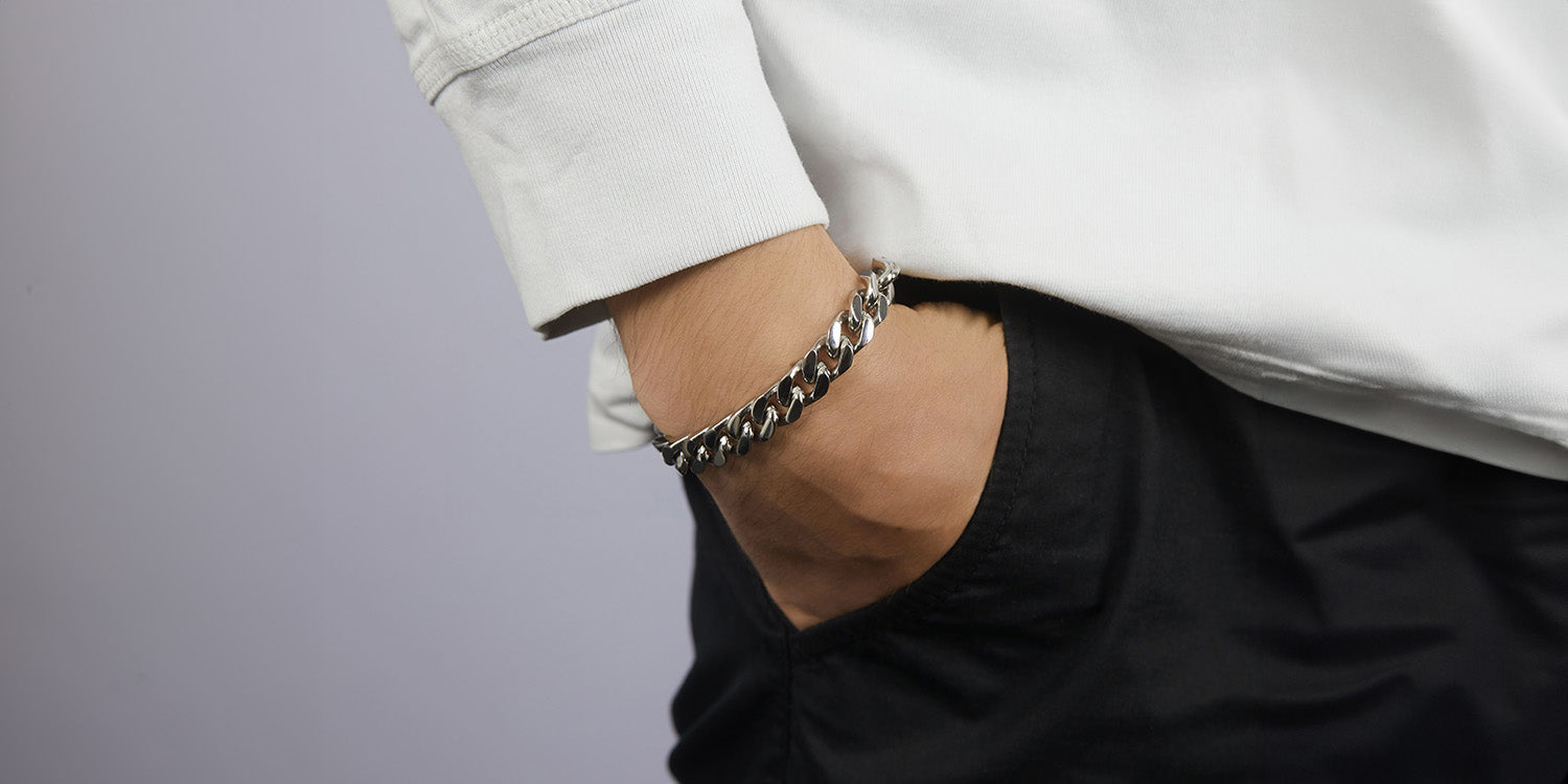 Mann mit Hand in Hosentasche trägt silbernes Panzerarmband in lässigem schwarz-weißen Outfit