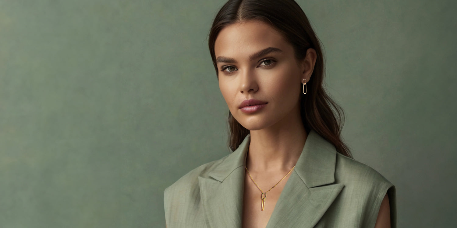 Elegante Frau in olivgrünem Blazer mit braunen Haaren trägt bronzene Halskette mit Anhänger und passende Ohrringe