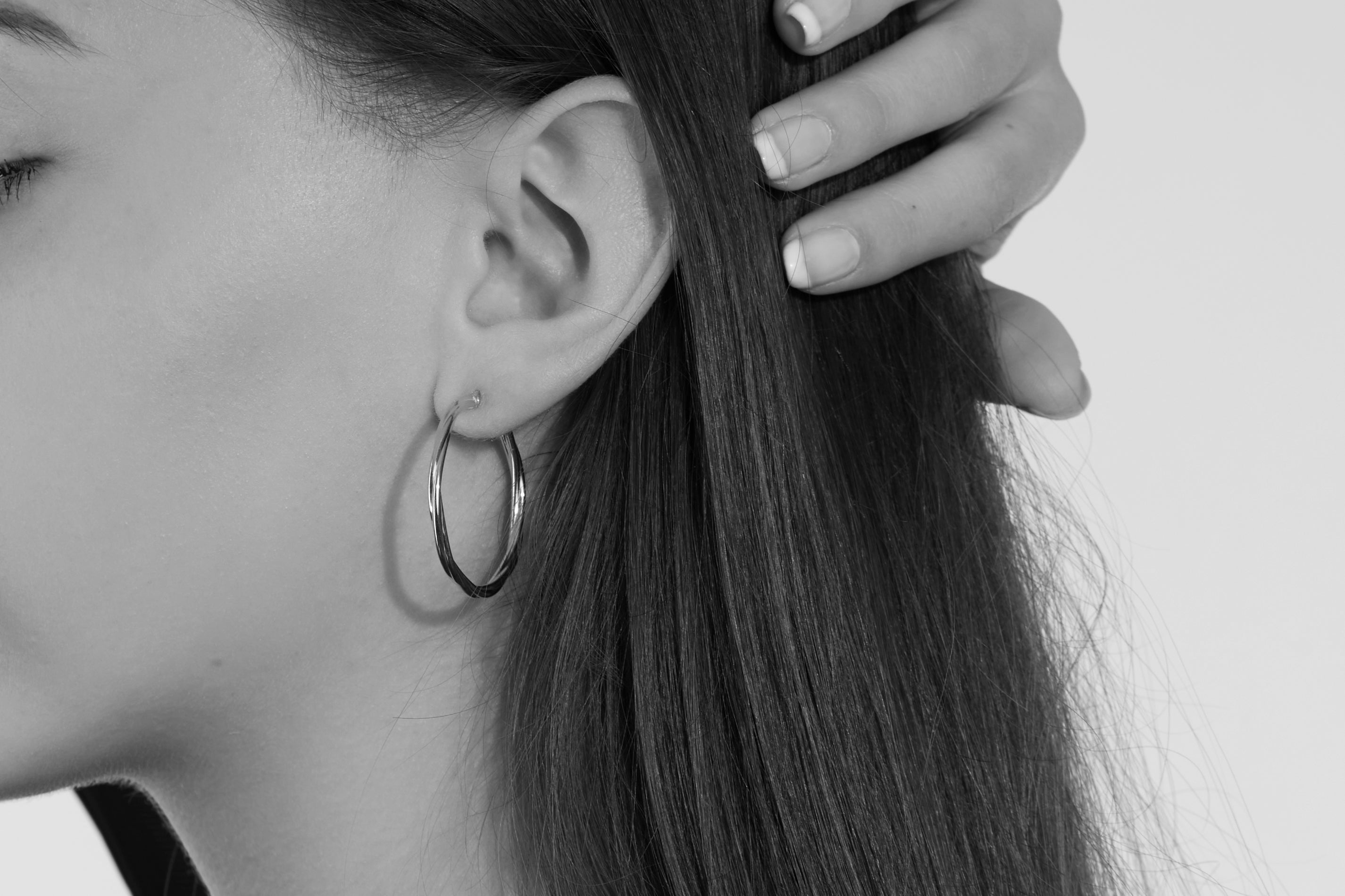 Frau mit dunklen Haaren trägt klassische silberne Creolen und fasst sich ins Haar in schwarz-weiß Aufnahme