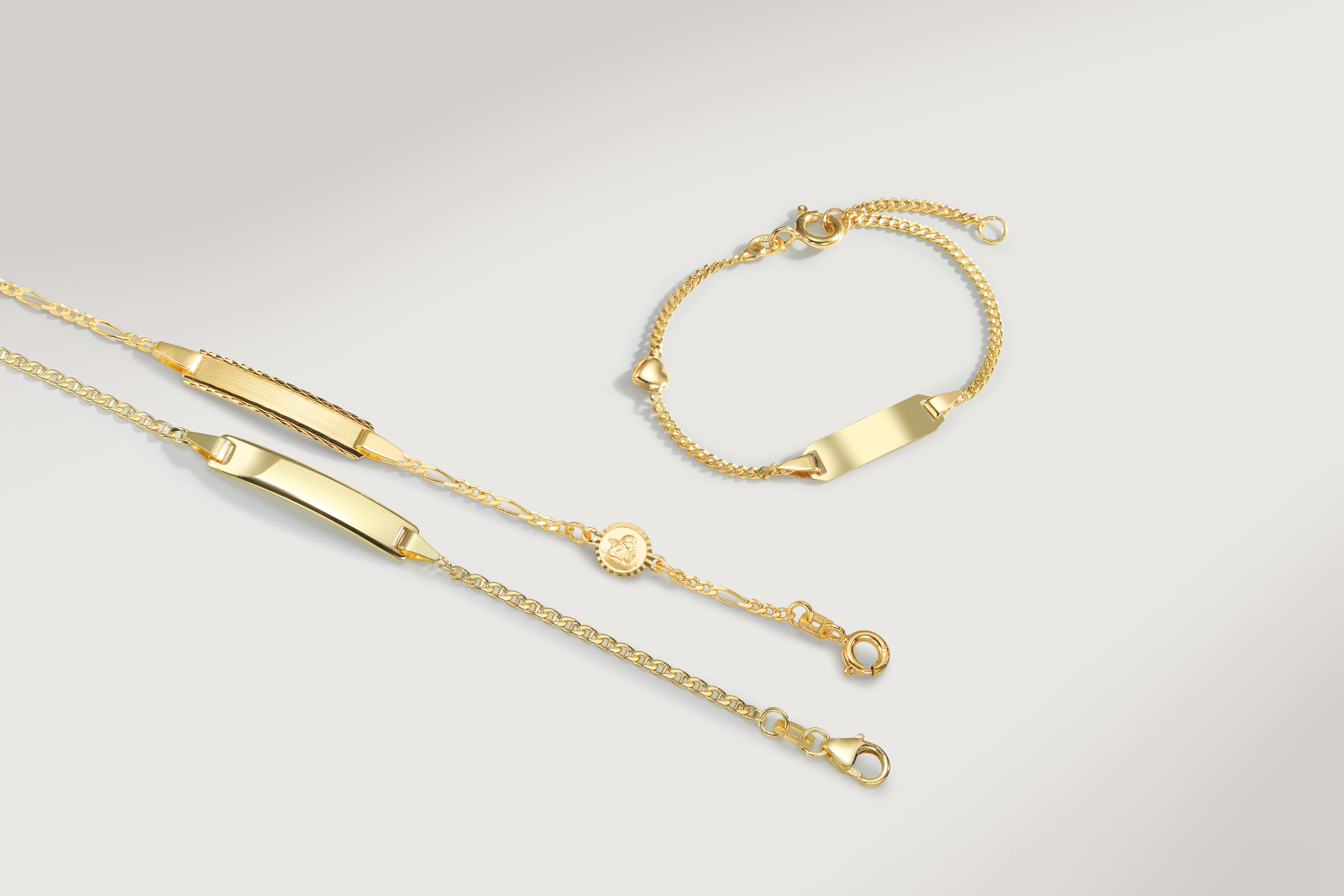 Goldene Kinderarmschmuck-Kollektion mit ID-Armbändern und Namensketten mit gravierbaren Schildchen auf hellem Hintergrund