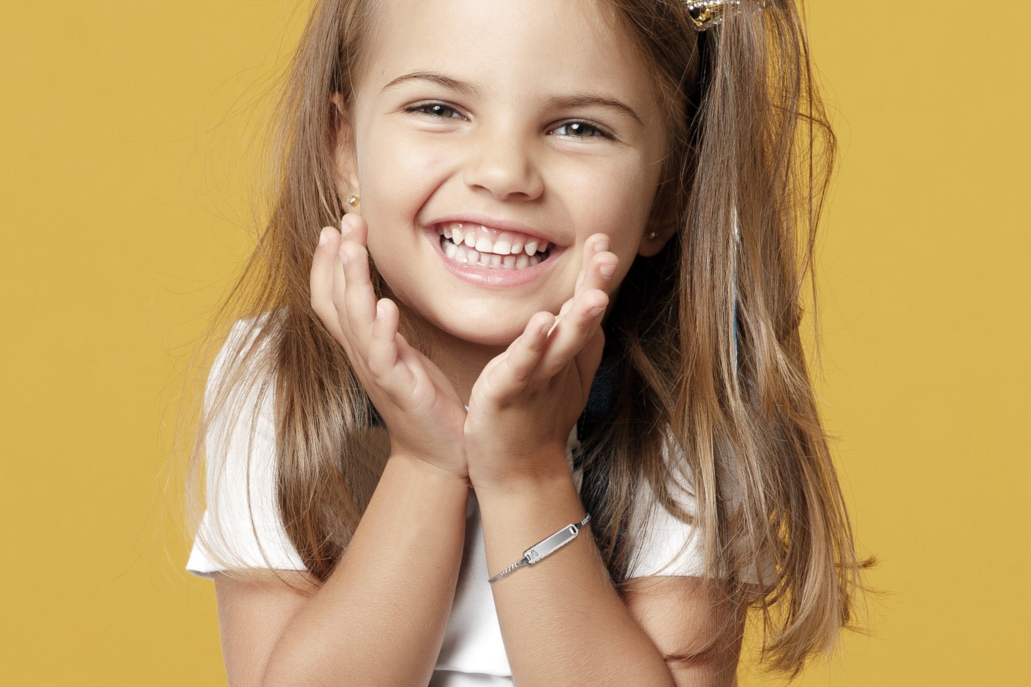 Fröhliches Mädchen mit blonden Haaren trägt ein silbernes Kinder-Gravurarmband und lächelt strahlend vor gelbem Hintergrund
